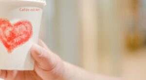 Eine Hand h&auml;lt einen Kaffeebecher mit einem roten Herz und der Aufschrift "Caf&eacute; mit Herz".