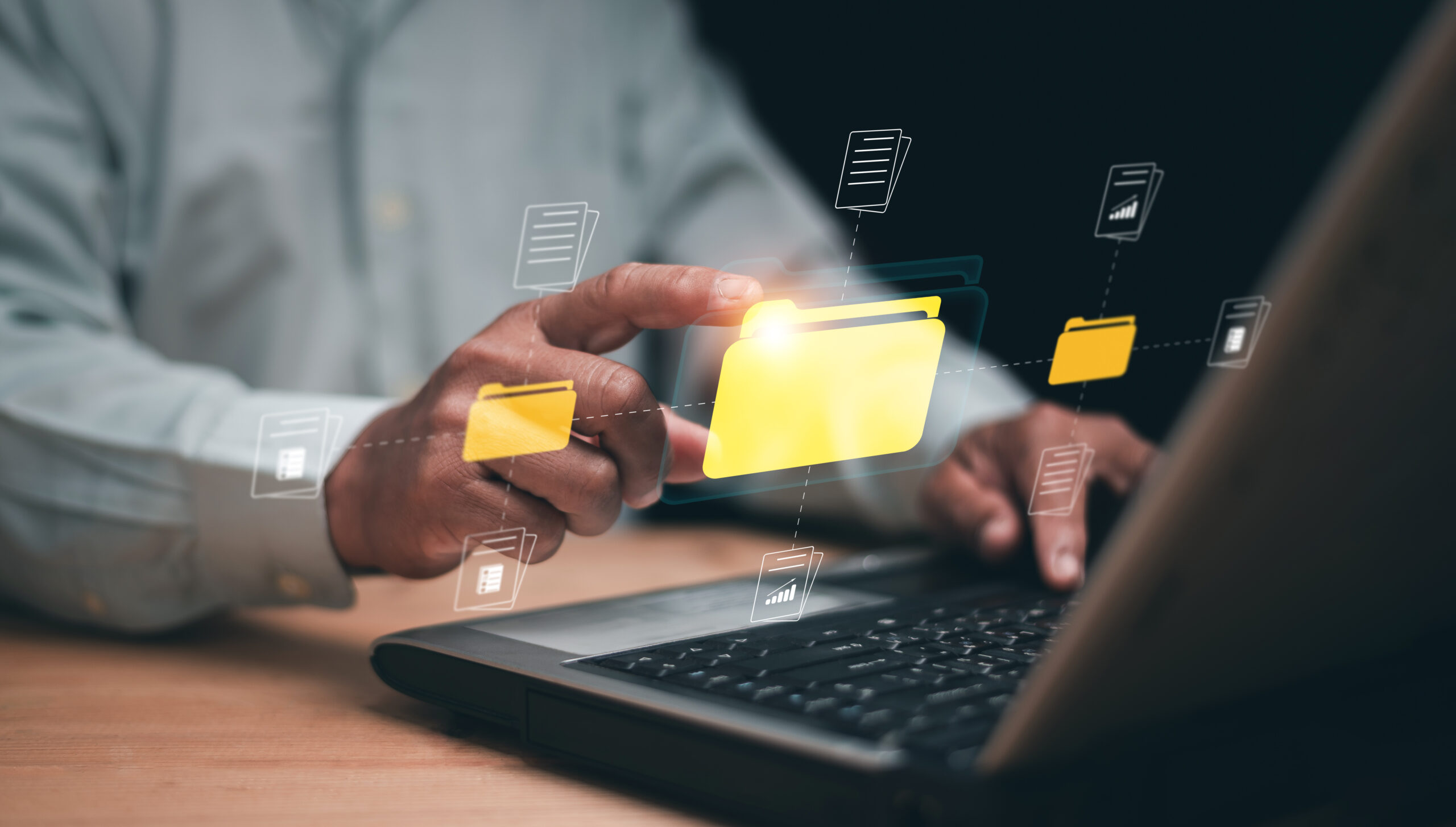Eine Hand zeigt auf ein digitales Ordnersymbol auf einem Laptop, umgeben von Daten-Icons.